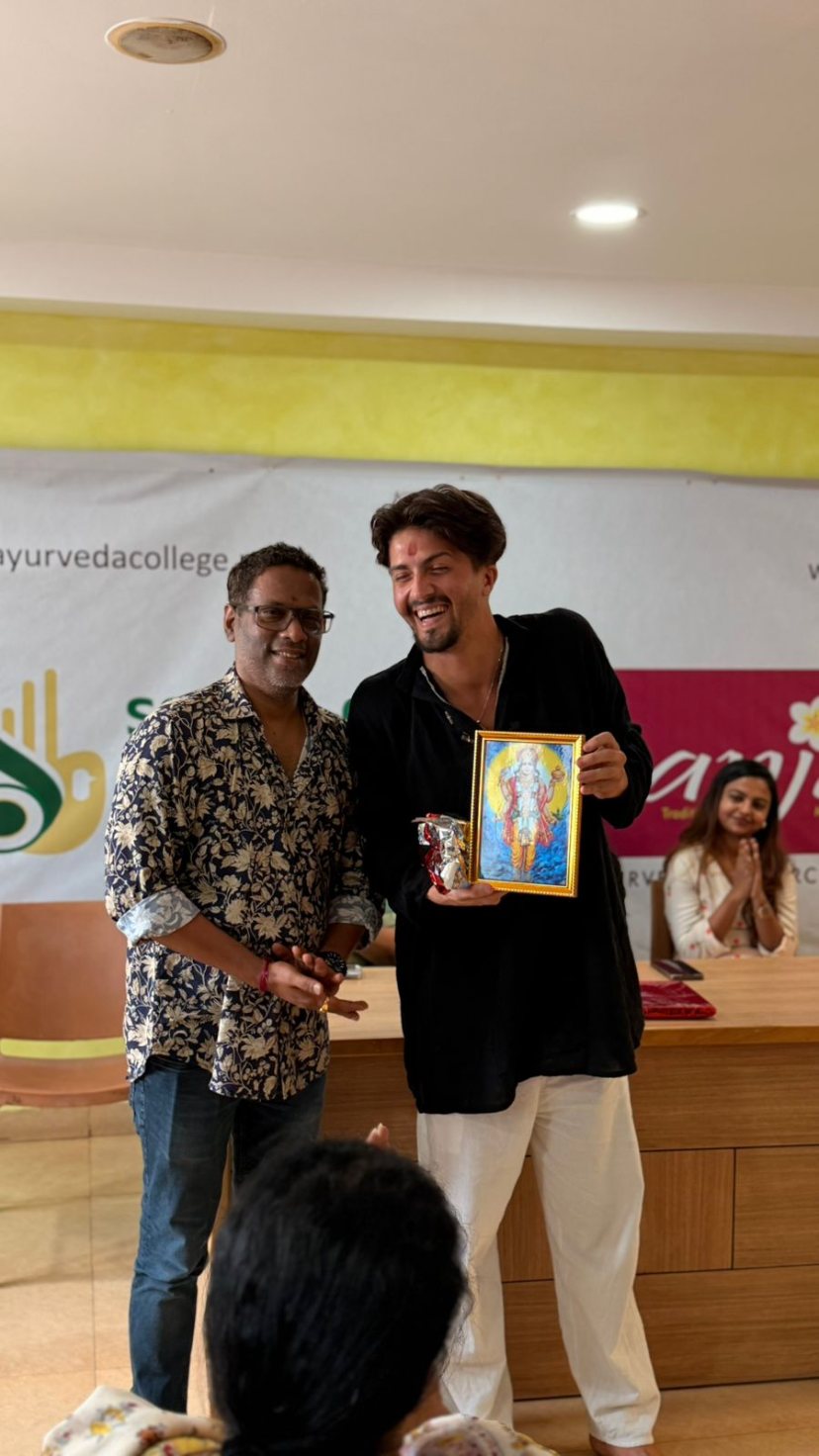 Dos personas sonriendo en un encuentro de una escuela de Ayurveda, sosteniendo un cuadro